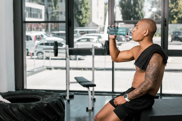 Seitenansicht muskulöser, hemdsloser afrikanisch-amerikanischer Sportler, der Wasser im Fitnessstudio trinkt — Stockfoto