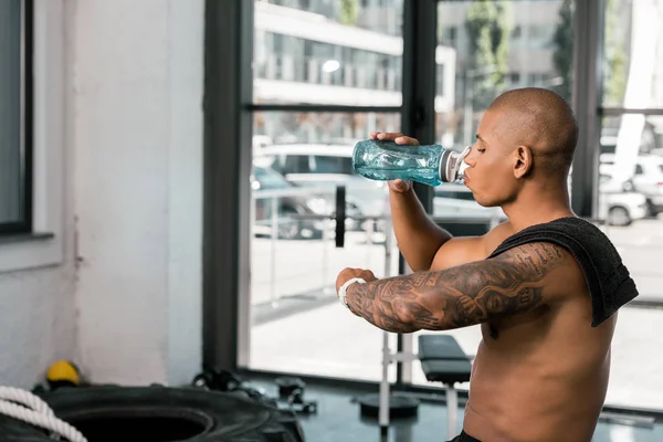 Seitenansicht eines jungen muskulösen Mannes, der Wasser trinkt und im Fitnessstudio Smartwatch checkt — Stockfoto