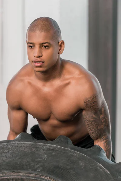 Concentrated young african american sportsman training with tyre in gym — Stock Photo