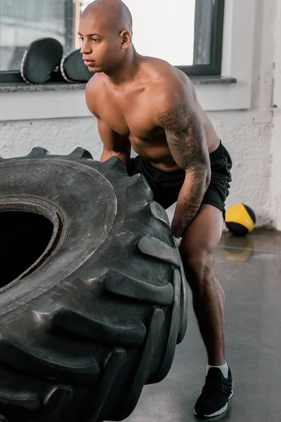 Muscular young african american man exercising with tyre in gym — Stock Photo