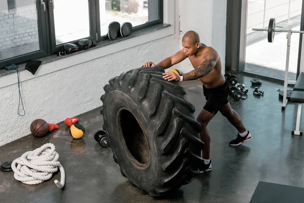 Aus der Vogelperspektive: muskulöser junger afrikanisch-amerikanischer Mann trainiert mit Reifen im Fitnessstudio — Stockfoto