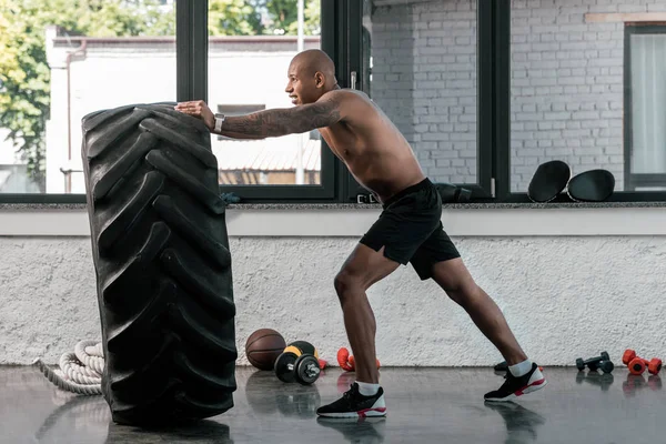 Vue latérale de l'entraînement musclé homme torse nu avec pneu dans la salle de gym — Photo de stock