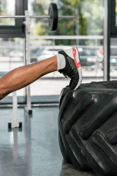 Cropped shot of muscular male leg on tire in gym — Stock Photo