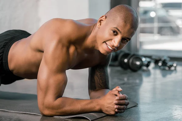 Fröhlicher afrikanisch-amerikanischer Sportler beim Planken auf Fitnessmatte im Fitnessstudio — Stockfoto