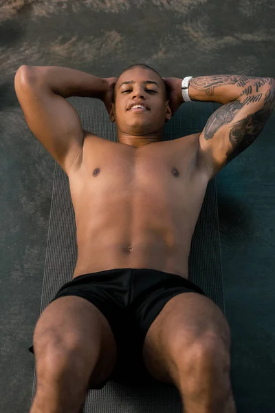 High angle view of tattooed african american sportsman doing abs on fitness mat at gym — Stock Photo