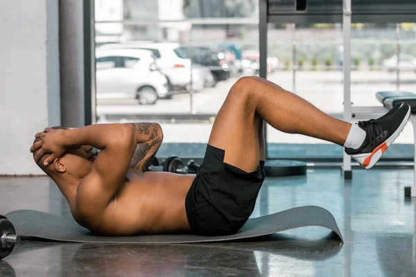 Боковой вид афроамериканца, делающего зарядку на фитнес-коврике в спортзале — стоковое фото