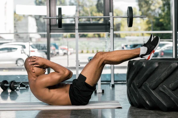 Seitenansicht eines afrikanisch-amerikanischen Mannes beim Bauchmuskeltraining auf einer Fitnessmatte im Fitnessstudio — Stockfoto