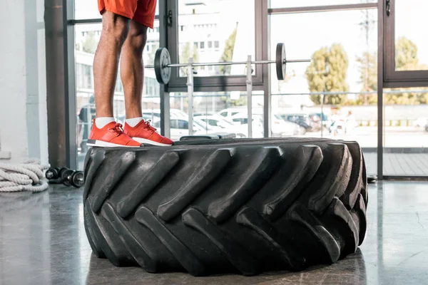 Cropped image of sportsman in sneakers standing on tire at gym — Stock Photo