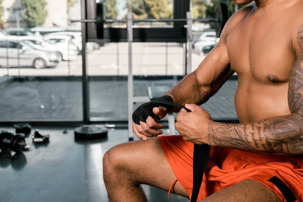 Visão parcial de tatuado desportista afro-americano envolvendo mão em bandagem de boxe no ginásio — Fotografia de Stock