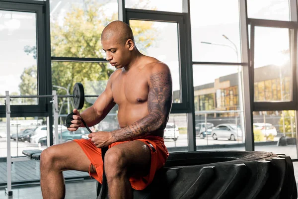 Shirtless african american sportsman wrapping hand in boxing bandage at gym — Stock Photo