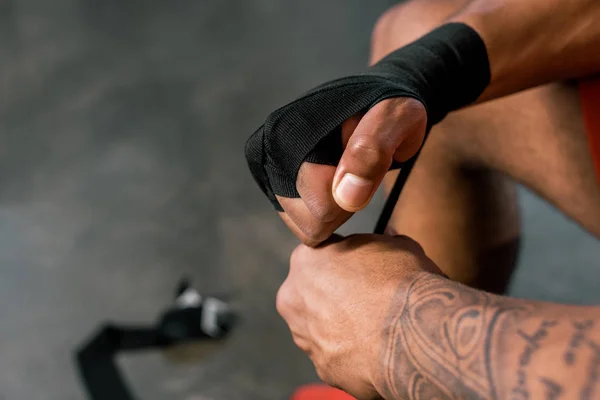 Imagen recortada de deportista tatuado envolviendo la mano en venda de boxeo en el gimnasio - foto de stock