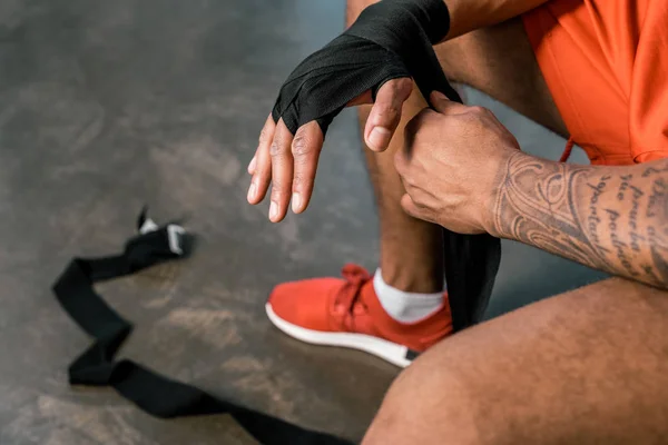 Teilansicht tätowierter afrikanisch-amerikanischer Sportler, der im Fitnessstudio die Hand in Boxverband wickelt — Stockfoto