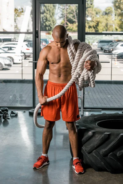 Uomo africano americano muscoloso senza maglietta con corda da battaglia in palestra — Foto stock
