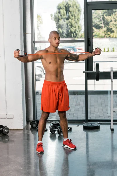 Muscular african american sportsman exercising with stretching band at gym — Stock Photo