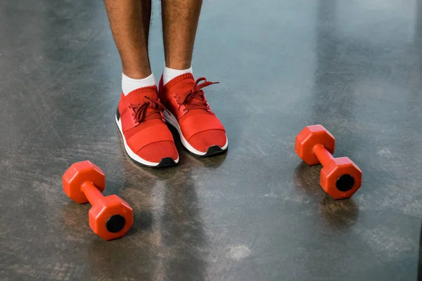 Unterteil eines Sportlers in roten Turnschuhen, der in der Nähe von Kurzhanteln auf dem Boden im Fitnessstudio steht — Stockfoto