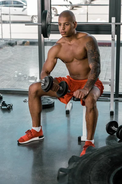 Deportista afroamericano tatuado haciendo ejercicio con mancuerna en el gimnasio - foto de stock