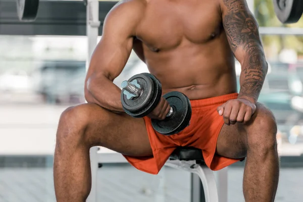 Abgeschnittenes Bild eines tätowierten afrikanisch-amerikanischen Sportlers, der im Fitnessstudio mit einer Hantel trainiert — Stockfoto