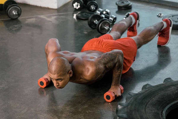 Selective focus of young african american sportsman doing push ups with dumbbells at gym — Stock Photo