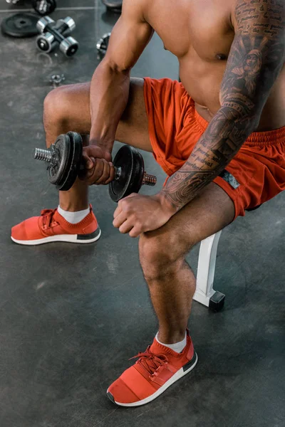 Vista parcial del atleta afroamericano tatuado haciendo ejercicio con mancuerna en el gimnasio - foto de stock