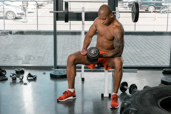 Tattooed muscular african american sportsman exercising with dumbbell at gym — Stock Photo