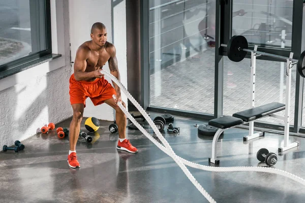 Vue grand angle de l'athlète afro-américain travaillant avec des cordes de combat à la salle de gym — Photo de stock