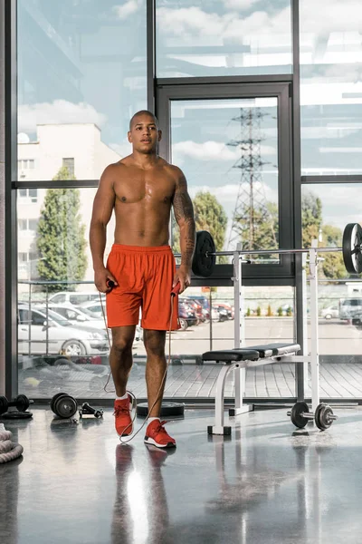 Atleta afroamericano muscoloso senza maglietta in piedi con corda da salto in palestra — Foto stock