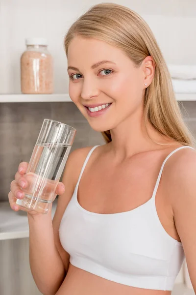 Primer plano retrato de la mujer embarazada con un vaso de agua mirando a la cámara en el baño - foto de stock