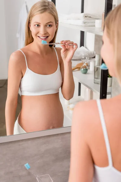 Mujer embarazada feliz mirando el espejo y cepillarse los dientes en el baño - foto de stock