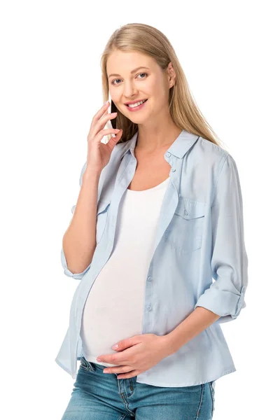 Hermosa mujer embarazada tocando el estómago y hablando en el teléfono inteligente aislado en blanco - foto de stock
