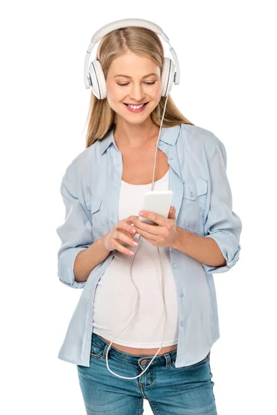Atractiva mujer embarazada escuchando música con auriculares y teléfono inteligente aislado en blanco - foto de stock