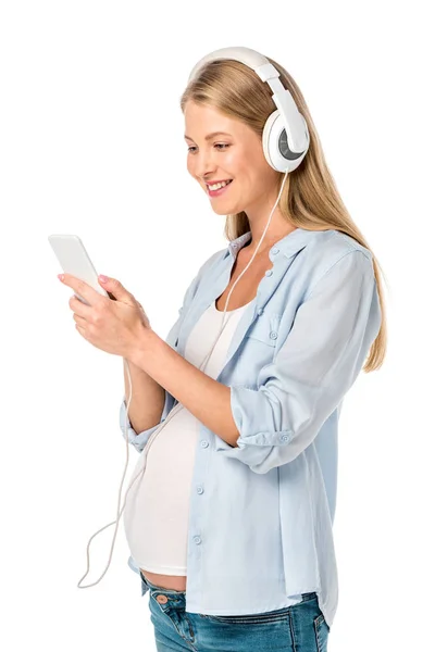 Felice donna incinta ascoltare musica con cuffie e smartphone isolato su bianco — Foto stock