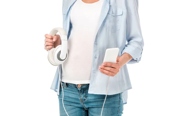 Vista cortada da mulher grávida segurando fones de ouvido e smartphone isolado no branco — Fotografia de Stock