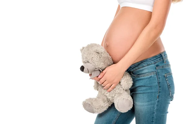 Vista ritagliata della donna incinta che tiene orsacchiotto vicino al ventre isolato su bianco — Foto stock