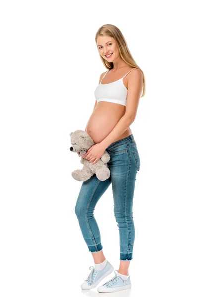 Hermosa sonriente embarazada sosteniendo osito de peluche aislado en blanco - foto de stock