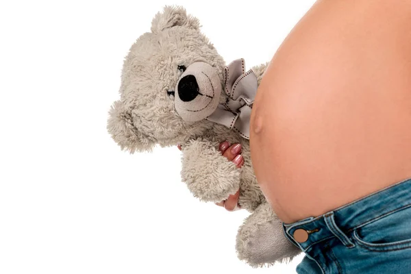 Крупный план беременной девушки, держащей плюшевого мишку на животе изолированы на белом — стоковое фото