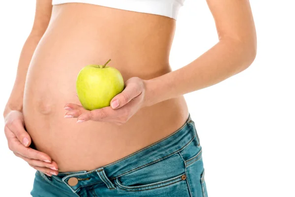 Обрезанный вид беременной женщины касаясь живота и держа зеленое яблоко изолированы на белом — стоковое фото