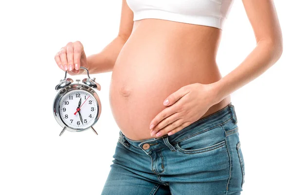 Midsection view of pregnant woman touching belly and holding alarm clock isolated on white — Stock Photo