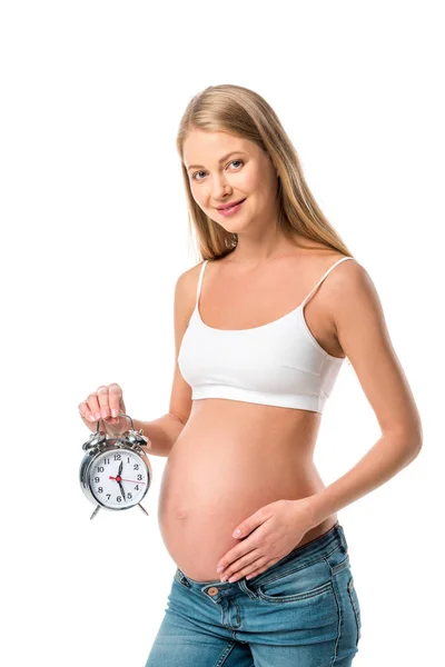 Pregnant woman in white bra holding alarm clock isolated on white — Stock Photo