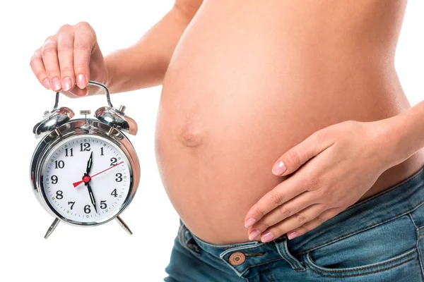 Vista recortada de la mujer embarazada tocando el vientre y la celebración de reloj despertador aislado en blanco - foto de stock