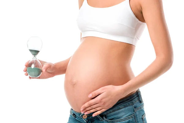 Vue recadrée de la femme enceinte touchant le ventre et tenant sablier isolé sur blanc — Photo de stock
