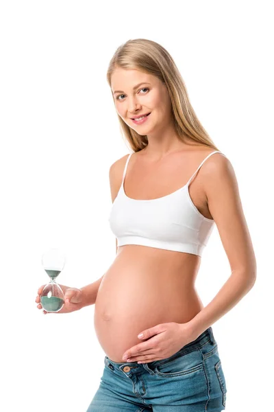 Atractiva mujer embarazada sosteniendo reloj de arena aislado en blanco - foto de stock