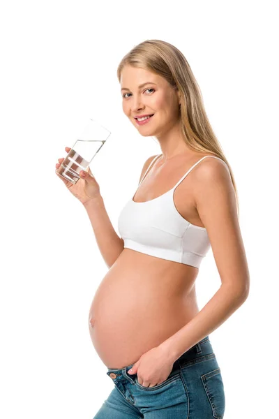 Mulher grávida sorridente em sutiã branco segurando vidro de água pura isolado em branco — Fotografia de Stock