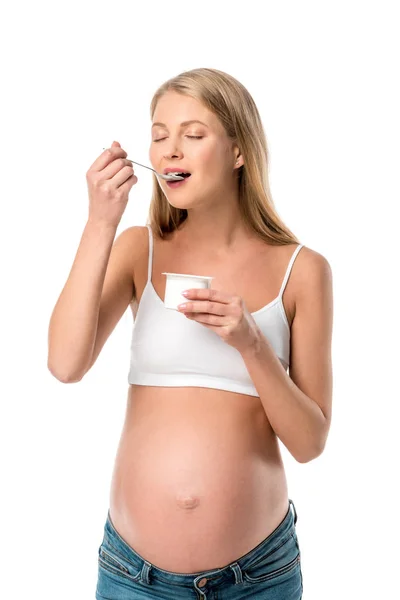 Atractiva mujer embarazada con los ojos cerrados comiendo yogur aislado en blanco - foto de stock