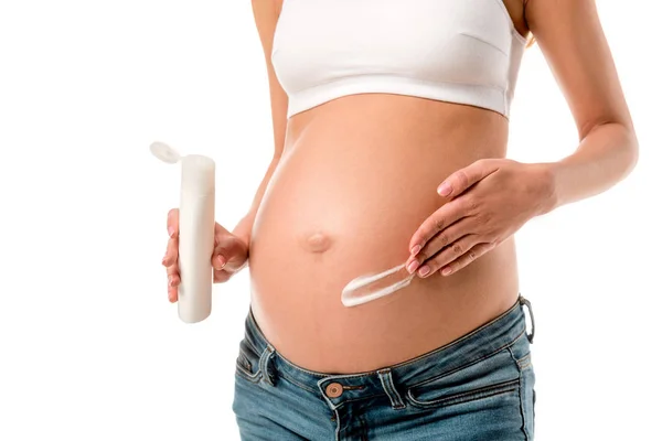 Обрізаний вид вагітної жінки, що наносить косметичний крем на живіт, щоб уникнути розтяжок ізольовані на білому — стокове фото