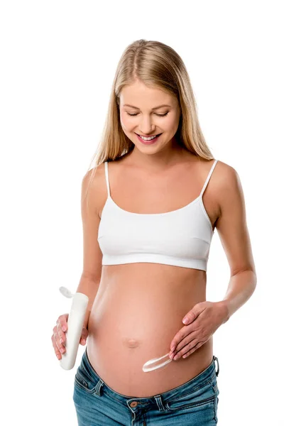 Приваблива вагітна жінка наносить лосьйон на живіт, щоб уникнути розтяжок ізольовані на білому — стокове фото