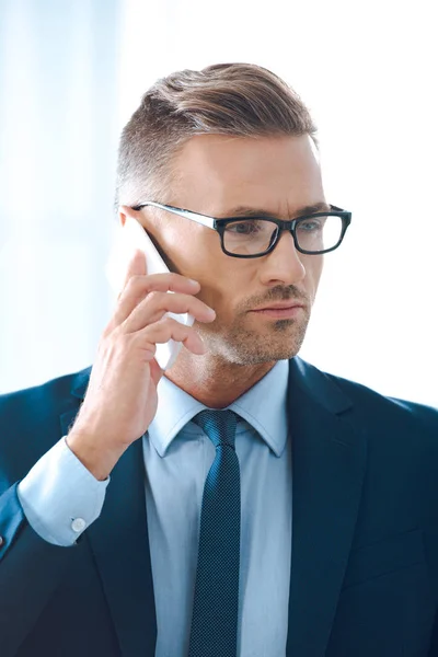 Красивий бізнесмен в окулярах розмовляє по смартфону і дивиться вбік — стокове фото