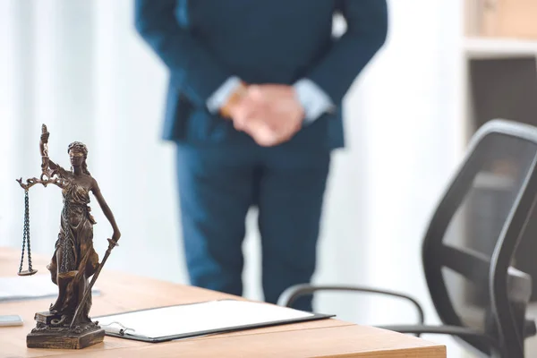 Vista ravvicinata della statua di giustizia signora e appunti sul tavolo e avvocato in piedi dietro — Foto stock