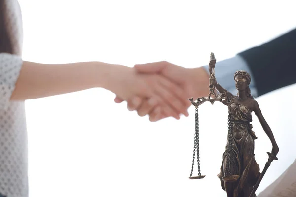 Vista de cerca de la estatua de la justicia dama y abogado con el cliente en blanco estrechando las manos detrás - foto de stock