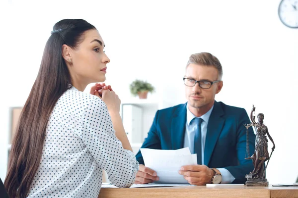 Avocat détenant des papiers et regardant jeune femme bouleversée dans le bureau — Photo de stock