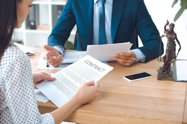 Recortado tiro de abogado celebración de papeles y cliente contrato de lectura en la oficina - foto de stock